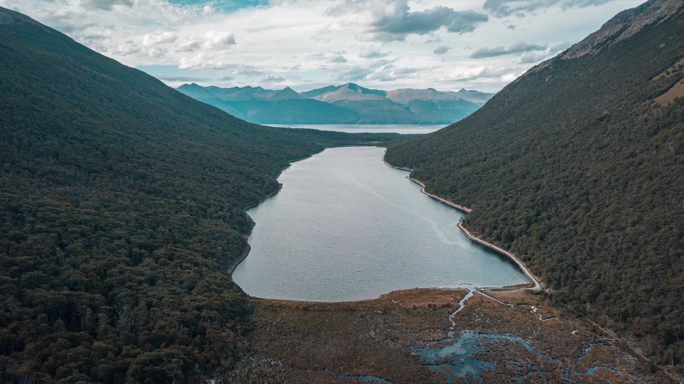 Lago alargado entre laderas de bosque fueguino, con la cordillera al fondo
