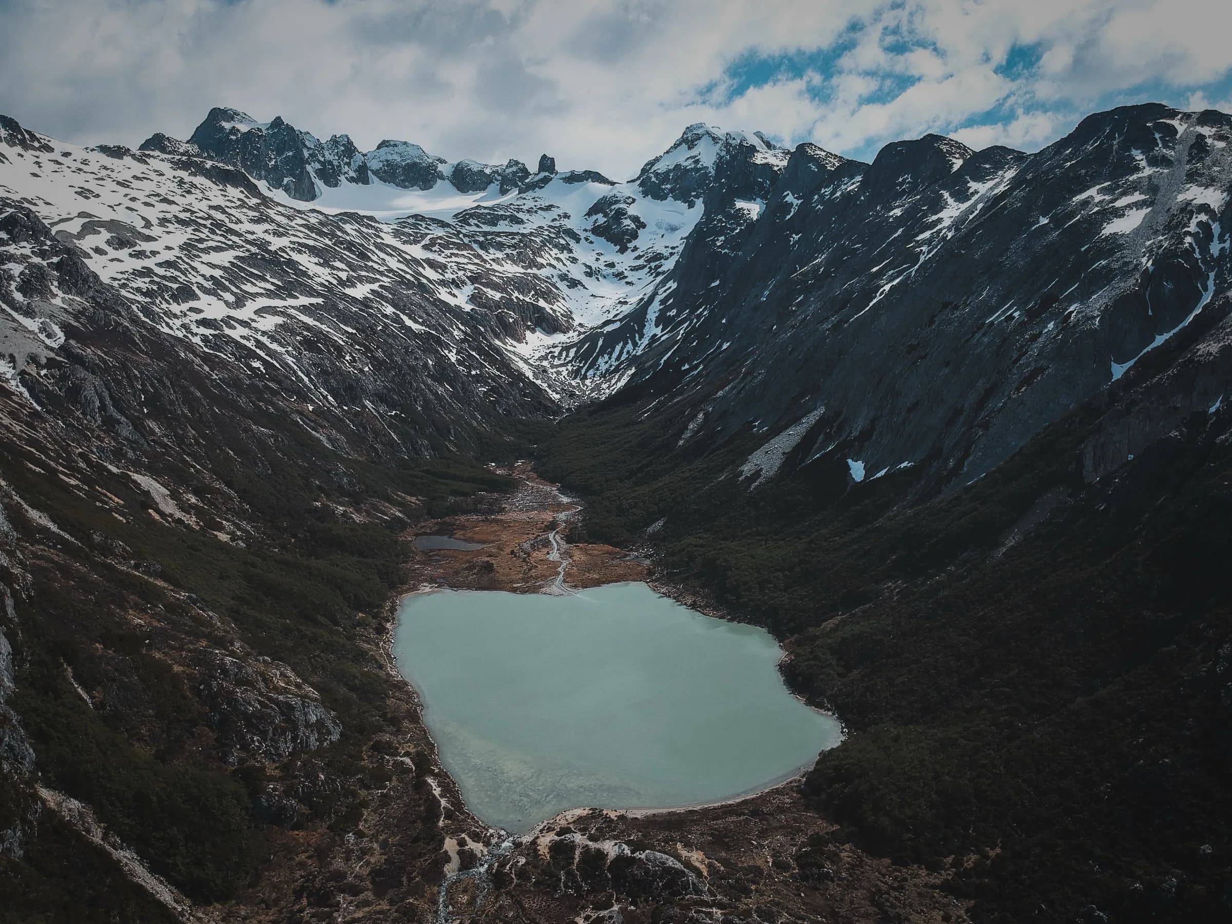 Laguna de origen glaciar encajada entre paredes de roca y nieve en los Andes fueguinos