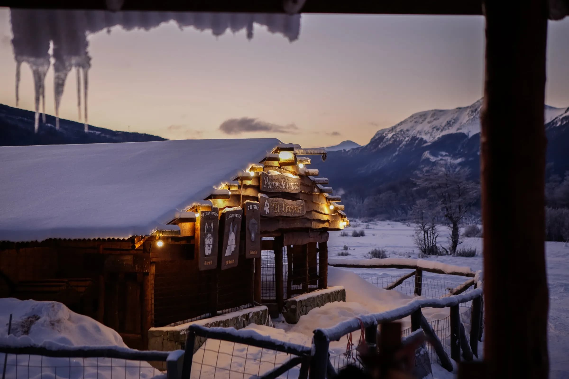 Refugio El Greyster iluminado al atardecer con carámbanos de hielo y montañas nevadas